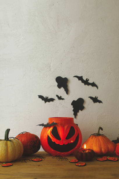 istock Jack of lantern candy bucket, pumpkins, black spiders, bats and ghosts decorations on rustic background in evening room. Spooky Halloween still life. Happy Halloween! Trick or treat! 1427445764