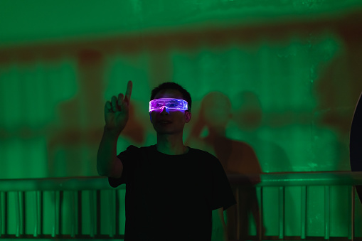 Man using smart glasses to experience virtual reality game on green light background