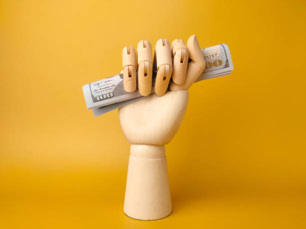 istock Wooden hand gripping banknotes on a yellow background. 1427460067