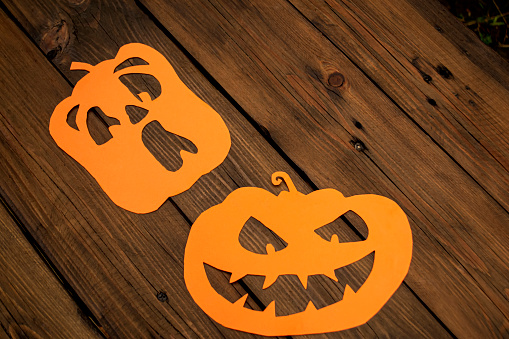 Two heads of jack lantern on a wooden table, jack lantern made of paper. Halloween pumpkins made of orange paper, top view.