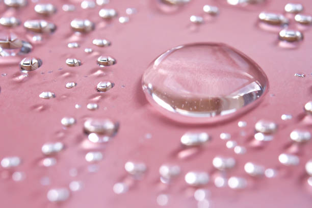 A large drop and splashes of micellar water on a pink background.
