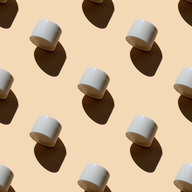 istock Seamless pattern of mockups of white plastic jars with moisturizer. Unmarked containers for lotion, cleanser, shampoo on beige background with shadows. Top view, flat lay 1427465372