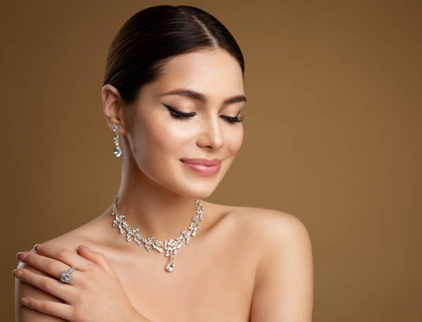 modelo de belleza en conjunto de joyas de boda. mujer elegante en collar con pendiente y anillo. hermosa chica con maquillaje de delineador de ojos perfecto y piel suave sobre fondo beige - women diamond gem precious gem fotografías e imágenes de stock