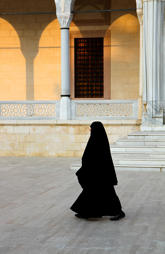 Adana, Turkey-July 24,2010: Religious Islamic Woman in Black Burka Outfit walking in front of Sabanci Central Mosque