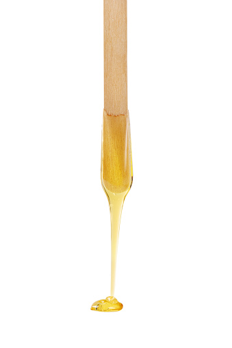 Golden sugar paste or wax for depilation dripping from wooden stick isolated on white background.