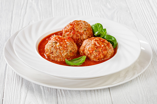 Italian Porcupine Balls, ground beef and rice meatballs in tomato sauce with basil leaves in white bowl, horizontal view from above