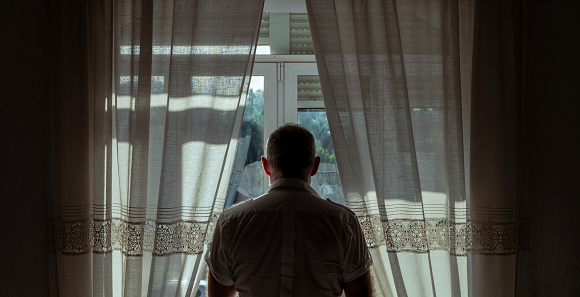 Vista trasera del hombre adulto de pie junto a la ventana con luz solar y sombra photo
