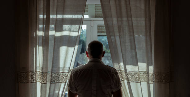 vue arrière d’un homme adulte debout à côté de la fenêtre avec la lumière du soleil et l’ombre - un seul homme photos et images de collection