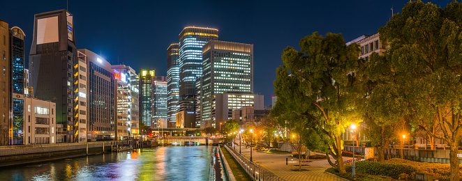 Glittering skyscrapers of downtown Osaka overlooking the tranquil waters of the Tasahori River illuminated at night, Japan.
