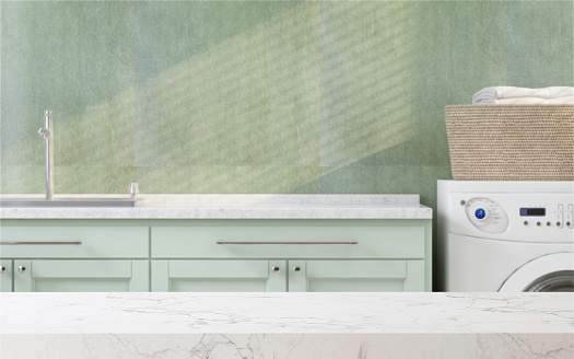 White marble tabletop or countertop in laundry utility room with built-in counter and washing machine, green wall with sunlight at home for household washing and cleaning product display