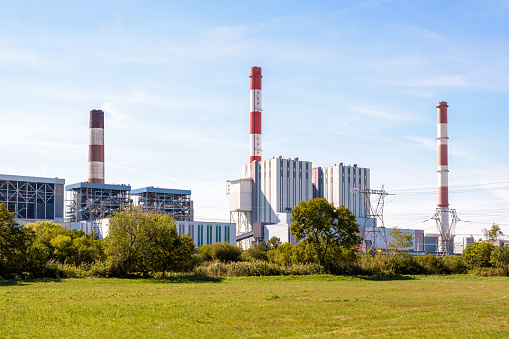 Cordemais, France - September 20, 2022: General view of the EDF coal-fired power station of Cordemais with its three red and white smokestacks, seen from the surrounding meadows on a sunny summer day.