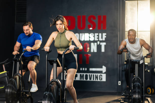 gruppo di giovani atleti che fanno esercizio insieme in palestra fitness. attraenti sportivi attivi si allenano insieme pedalando su una macchina da bici per l'assistenza sanitaria e il benessere nello stadio. - spinning health club instructor gym foto e immagini stock