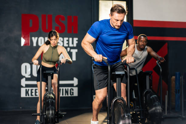 gruppo di giovani atleti che fanno esercizio insieme nella palestra fitness. attraenti sportivi attivi e sportivi si allenano insieme pedalando su una macchina da bici per l'assistenza sanitaria e il benessere nello stadio. - spinning health club instructor gym foto e immagini stock