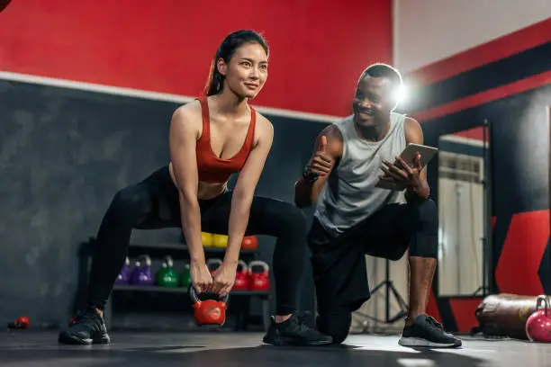 African American trainer motivate young sportsgirl to exercise in gym. Instructor coach teach Caucasian girl lift weight dumbbell for biceps to improve strength and maintain muscle at fitness club.