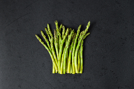 Fresh green asparagus in eco mesh bag on black slate background. Top view copy space.