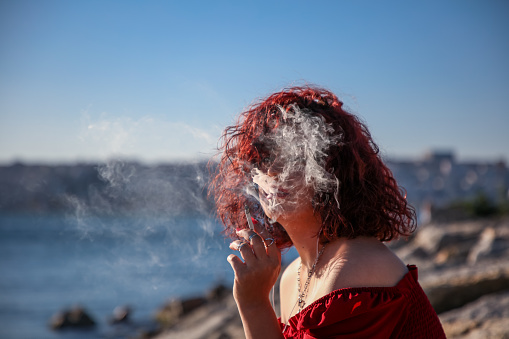 Young girl with red hair smoking on the beach