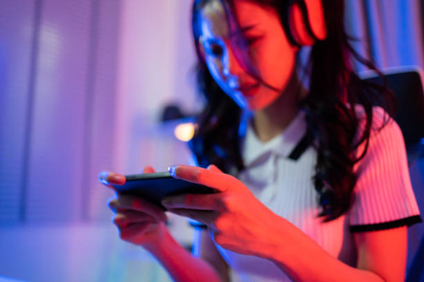 Asian beautiful Esport woman gamer play online mobile game on computer. Attractive young girl gaming player feel happy, enjoy technology broadcast live streaming while plays cyber tournament at home. stock photo