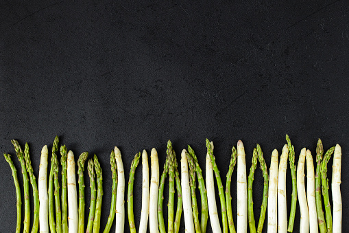 Fresh white and green asparagus on black slate background. Top view copy space.