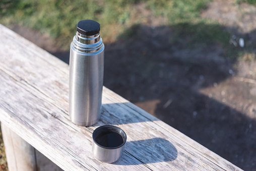 pouring tea  from thermos near by a lake