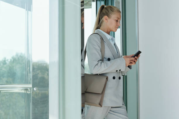 istock Serious young blond female employee texting in smartphone in elevator 1427499244