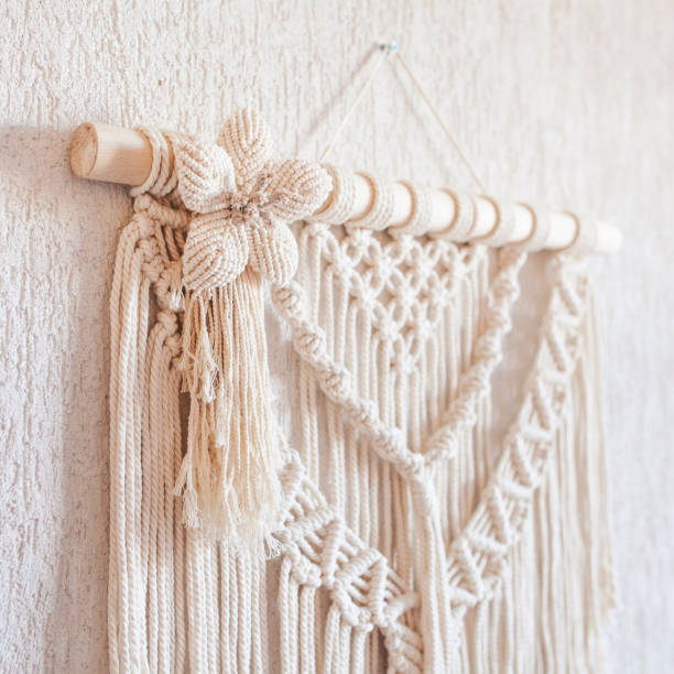 istock Handmade macrame wall decoration with wooden stick hanging on a white wall. Macrame braiding and cotton threads. Female hobby. ECO friendly modern knitting natural decoration in interior 1427499694
