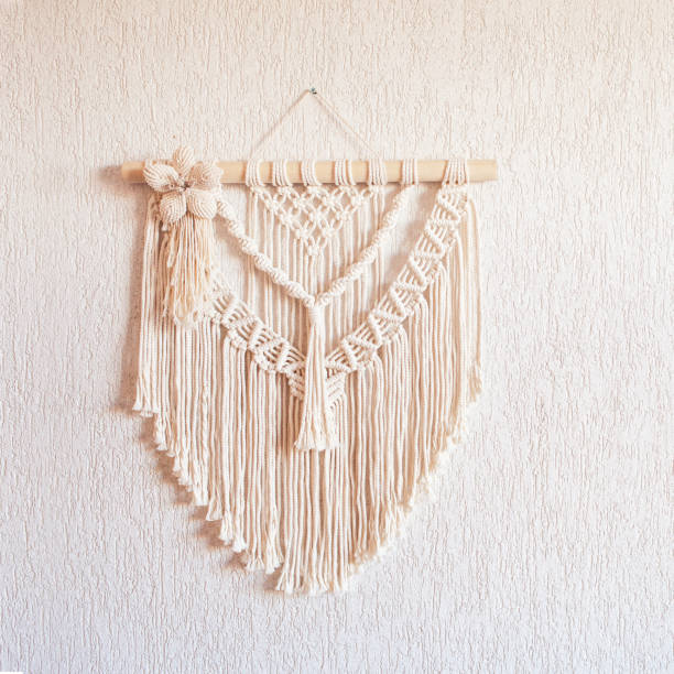 istock Handmade macrame wall decoration with wooden stick hanging on a white wall. Macrame braiding and cotton threads. Female hobby. ECO friendly modern knitting natural decoration in interior. Copy space 1427499709