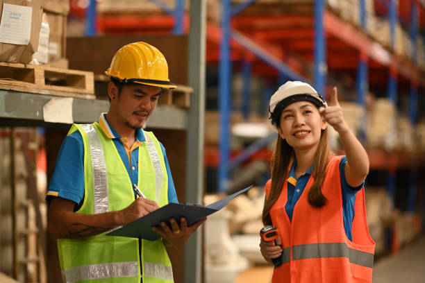 istock Warehouse workers wearing hardhats and reflective jackets using digital tablet, checking stock and order details in warehouse. 1427500410
