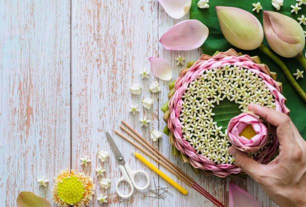 Pink lotus petal krathong for Thailand Loy Krathong festival decorates from lotus, crown flower, incense stick and candle Pink lotus petal krathong for Thailand Loy Krathong festival decorates from lotus, crown flower, incense stick and candle with blurred focus of hand holding lotus flower on wooden background. krathong stock pictures, royalty-free photos & images