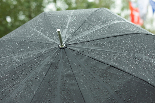 Black umbrella in rain. Large umbrella in bad weather. Raindrops on black material. Grass umbrella on street.