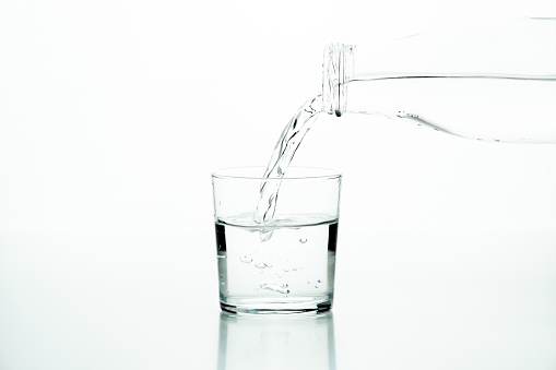 Fresh cold water in a glass. Clean shoot on blue background. Flowing water from high up into a tall glass.