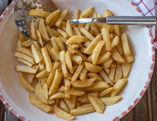 Delicious homemade  french fries. Served ready to eat in a big bowl isolated on wooden background. Closeup and table  top view