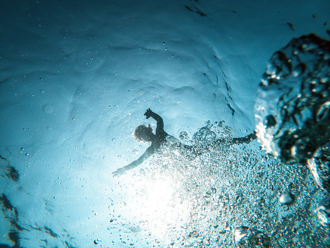 Underwater shot of a small kid floating in the sea. Water bubbles in the foreground. Backlight shot.