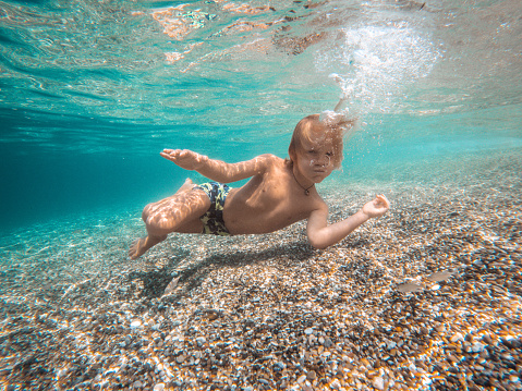 Cool White kid holding his breath underwater. He is playing on the shore in a beautiful beach.