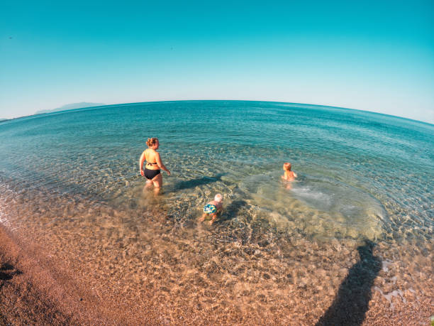 High angle view of a young Caucasian mother at the beach with her two little boys. They are happy, enjoying a blissful summer day.