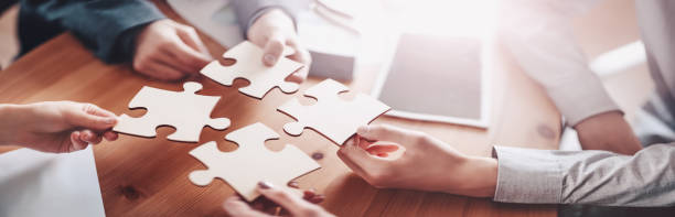 Businesswomen and businessmen working together while putting together puzzles. stock photo