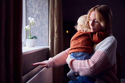 Madre con hijo tratando de mantenerse caliente por radiador en casa durante la crisis energética del costo de vida photo