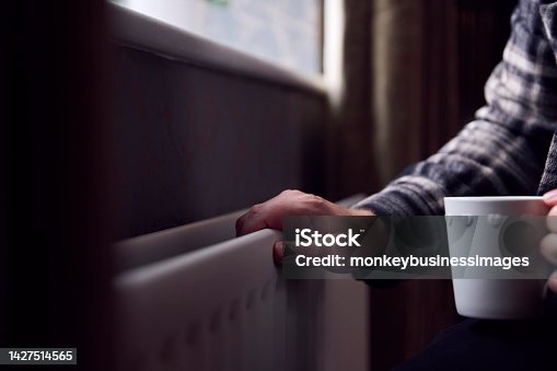 istock Close Up Of Mature Man Trying To Keep Warm By Radiator At Home During Cost Of Living Energy Crisis 1427514565