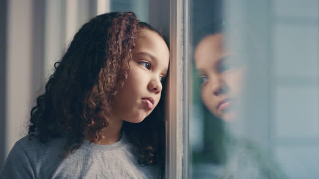 Depression, sad or mental health orphan by window in house interior, children home or autism orphanage community room. Zoom on thinking girl, face or lonely kid with stress or anxiety in social care