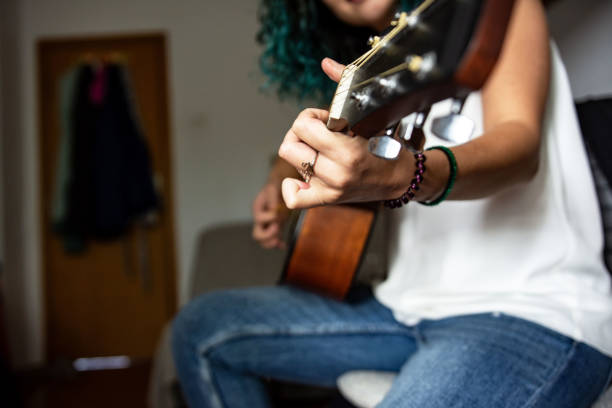 Unrecognizable beautiful young woman playing guitar at home