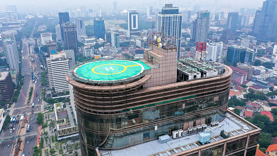 Aerial drone view of helipad on the roof of a skyscraper iin downtown with cityscape view on sunny day.