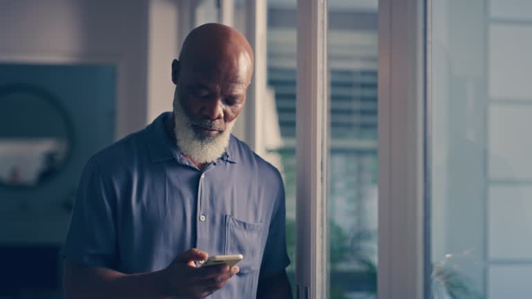 Stress, depression and elderly man texting on phone, sad and worried while looking out a window. Senior male feeling lonely, checking messages and fear, unhappy and confused by internet or app issue