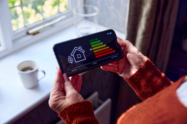 senior woman with smart meter trying to keep warm by radiator during cost of living energy crisis - power saving imagens e fotografias de stock