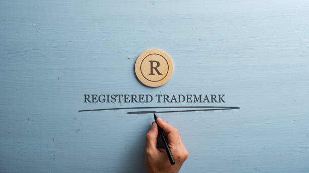 Letter R cut into wooden cut circle and male hand writing a Registered trademark sign under it stock photo