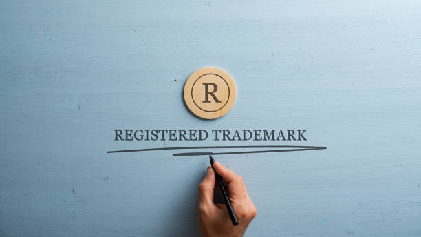 Letter R cut into wooden cut circle and male hand writing a Registered trademark sign under it Letter R cut into wooden cut circle and male hand writing a Registered trademark sign under it. Over pastel blue wooden background. patent stock pictures, royalty-free photos & images