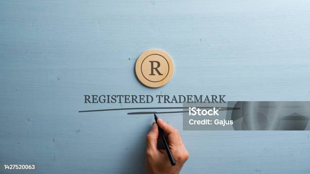 Letter R Cut Into Wooden Cut Circle And Male Hand Writing A Registered Trademark Sign Under It Stock Photo - Download Image Now