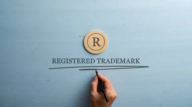 Photo of Letter R cut into wooden cut circle and male hand writing a Registered trademark sign under it