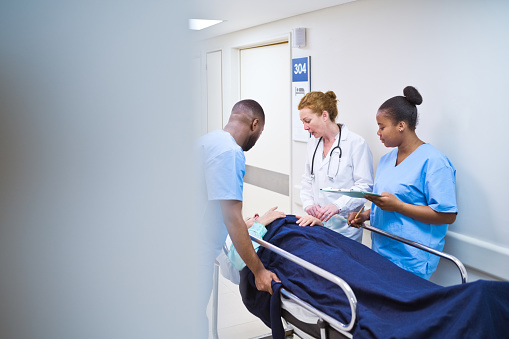 Female doctor discussing with nurses while examining patient lying on stretcher in hospital