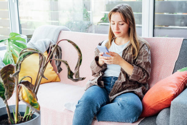 istock Young woman using mobile phone for searching info about houseplants disorders, it's identification and treatment for dried, sunburn leaf of potted plant Calathea. Houseplants diseases. Home gardening. 1427522473