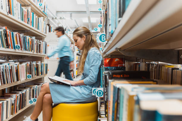 istock Young woman reading a book in the library 1427523843