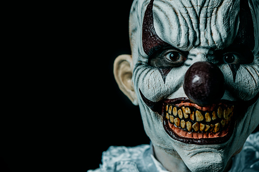 a creepy bald evil clown stares at the observer, against a black background with some blank space on the left